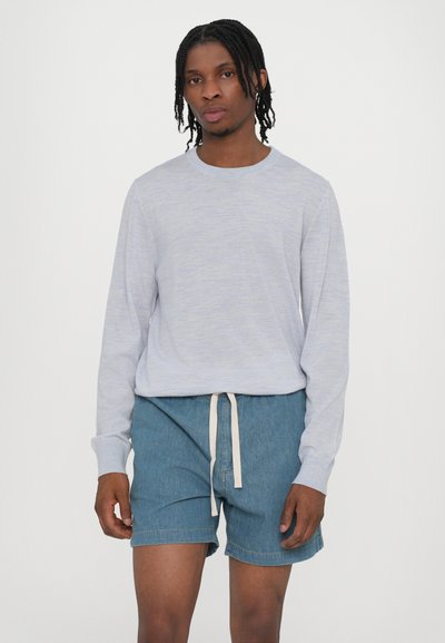 Chemise à manches longues gris clair en tissu doux, associée à un short en jean bleu avec un cordon blanc et des ourlets roulés.