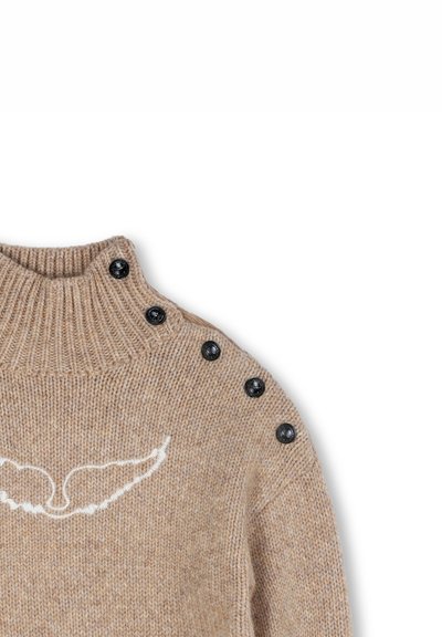 Pull en maille beige avec un col montant, accents de boutons noirs sur une épaule et broderie blanche en forme d'aile sur le devant.