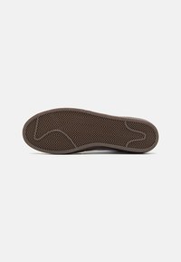 Suela de zapato de goma marrón con un patrón de relieve en zigzag. Bordes suaves y una ligera curva en la zona de los dedos. Diseño ligero y flexible.