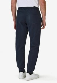 Tummansiniset jogginghousut, joissa on kapeampi istuvuus, joustava vyötärö ja takatasku. Materiaali näyttää pehmeältä ja hieman teksturoidulta. Yhdistetty valkoisiin lenkkareihin.