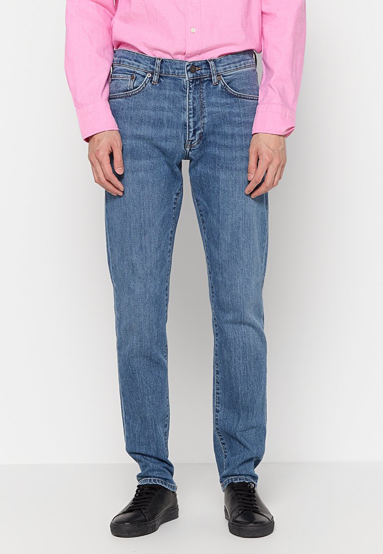 Jeans de mezclilla azul claro con un diseño de pierna recta, estilo de cinco bolsillos y sutiles detalles de desgaste. Llevados con una camisa de botones rosa.
