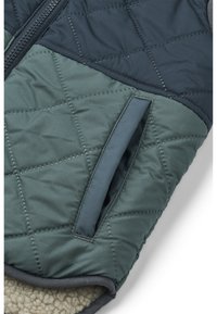 Gepolsterte Weste in Dunkelgrün und Navy, mit glatter Textur, Frontreißverschluss und einer Seitentasche mit weichem Fleece-Innenfutter.