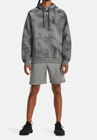 Felpa sportiva grigia con un motivo discreto, tasca a marsupio, cappuccio con cordino; abbinata a pantaloni corti grigi coordinati e sneakers nere.