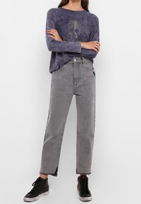 Lila Langarmhemd mit Schädelmotiv, kombiniert mit grauen weiten Jeans und schwarzen Sneakern. Ausgefranste Säume und seitliche Akzente an den Jeans.