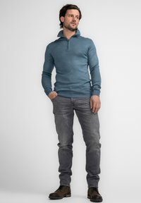 Blauwe kwart-rits pullover van breimateriaal, gecombineerd met grijze jeans en bruine veterschoenen. Heeft een aansluitend ontwerp en ribbelafwerkingen.