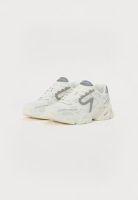 Zapatillas blancas con detalles en gris, con una parte superior texturizada, cierre de cordones, cuello acolchado y una suela de goma gruesa. Marca en la lengüeta.