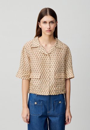 Blouse à manches courtes en beige avec un motif floral, dotée d'un col à revers et de deux poches avant, associée à un pantalon en denim bleu.