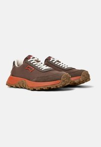 Sneaker marroni con una intersuola arancione, tessuto texturizzato, lacci bianchi e suola in gomma seghettata. Marchio discreto in rosso sulla linguetta.