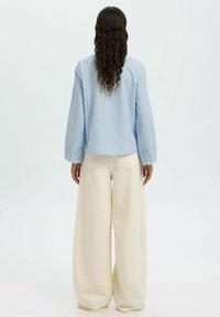 Heleheles sinine pikkade varrukatega särgiga, millel on silmaaugud varrukaotsas, kombineerituna kreemiate lõdvade pükstega. Sile tekstuur, mugav istuvus.