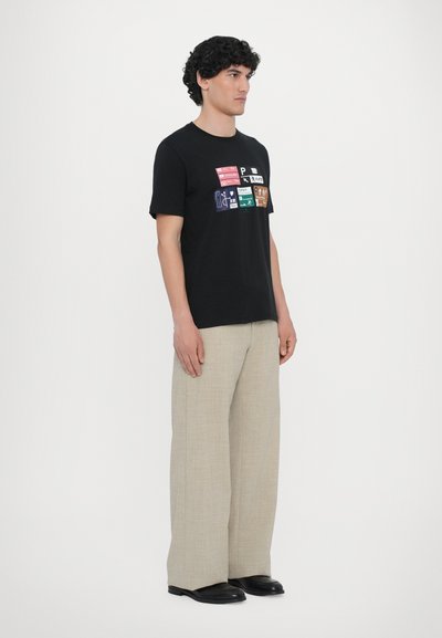 T-shirt en coton noir avec des imprimés graphiques colorés sur le devant. Assorti avec un pantalon large beige et des chaussures noires.