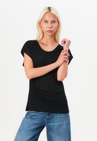 Black short-sleeve top with a round neckline, smooth texture, and a relaxed fit. Worn with light blue jeans.