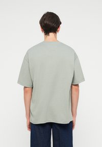 Tricou oversized de culoare verde deschis, cu mâneci scurte, decolteu rotund și textură fină din bumbac. Vederea din spate arată un design simplu, fără modele sau accente.