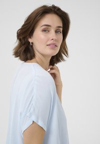 Haut à manches courtes bleu clair avec une finition douce et texturée. Le tissu tombe délicatement, offrant une coupe décontractée et des manches légèrement retroussées.
