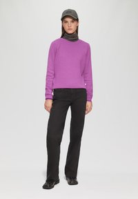 Lila strukturierter Pullover, schwarze Hose, verzierte schwarze Schuhe und eine graue Mütze. Einfaches Design, taillierte Passform mit gerippten Bündchen und Kragen.