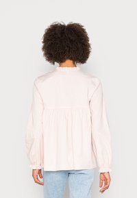 Blusa rosa claro de manga larga con escote con volantes y puños elásticos, que presenta una cintura fruncida para un ajuste holgado.