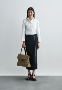 White fitted button-up shirt, black skirt with a side zipper, and a brown suede bag. Model wears burgundy shoes with a buckle detail.