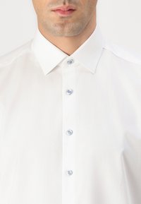 White dress shirt with a textured finish, pointed collar, and light blue buttons, featuring a fitted design and a smooth fabric.