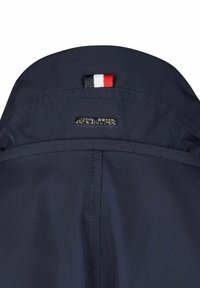Navyblauwe stoffen jasje met kraag en gestikte details. Bevat een klein driekleurig vlaggetje en een metalen merkembleem op de achterkant.