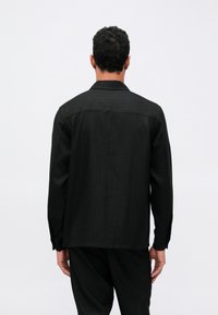 Svart langermet skjorte med rett snitt, med vertikale striper, krage og strukturert skulderdetalj.