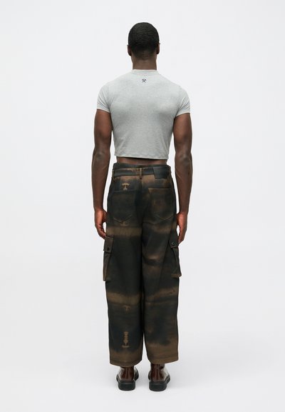 Pilkas trumpas marškinėliai ir juodos krovinių kelnės su rudos ir oranžinės spalvos dažų raštais. Kelnės turi šoninius kišenes ir yra šiek tiek laisvos.