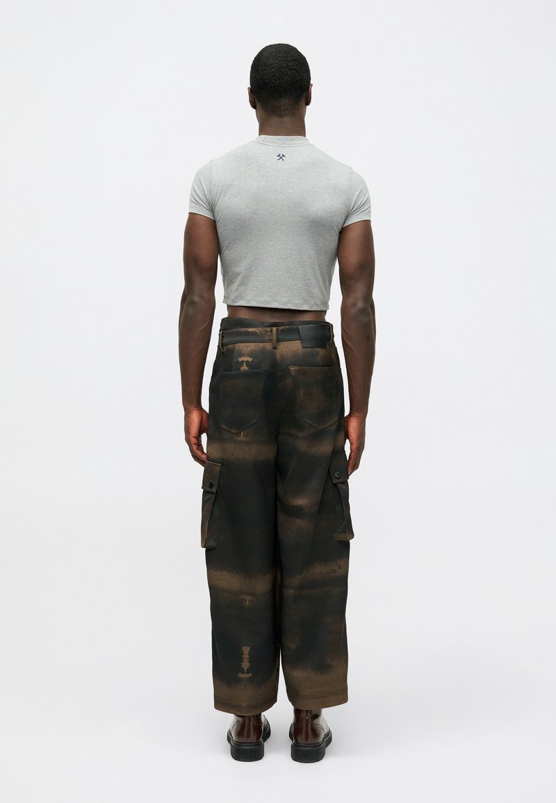Grijze cropped t-shirt en zwarte cargobroek met bruine en oranje verfpatronen. De broek heeft zijzakken en een iets losse pasvorm.