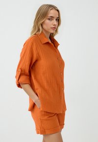 Oranje, gestructureerde katoenen shirt met een knoopsluiting aan de voorkant en opgerolde mouwen, gecombineerd met bijpassende shorts met omgeslagen manchetten.