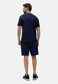 Conjunto de camiseta de algodón azul marino y pantalones cortos, que presenta un cuello redondo, mangas cortas y bolsillos tipo carga en los pantalones cortos.