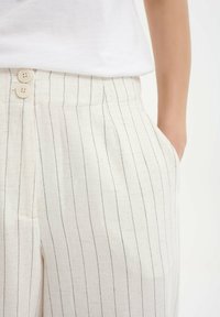 Lichtgekleurde linnen broek met dunne zwarte strepen, voorzien van twee knopen in de taille en zijzakken. Gestructureerde stof, relaxte pasvorm.