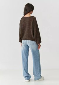 Brązowy sweter z dzianiny o szerokim dekolcie i prostym kroju, w zestawieniu z jasnoniebieskimi dżinsami z wysokim stanem i białymi sneakerami.