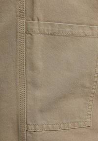 Beige kangas, jolla on sileä pinta, ja sivussa on ommeltu tasku. Yksinkertainen muotoilu, vahvistetut saumat kestävyyden parantamiseksi.