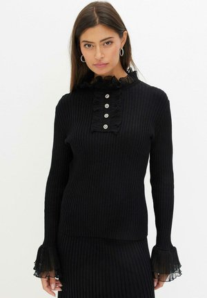 Haut noir à manches longues côtelé avec un col festonné, détail de bouton à l'avant et des poignets en tulle festonnés. Texture douce.