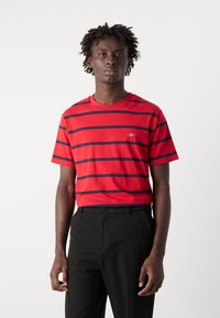 Rød kortærmet t-shirt med marineblå vandrette striber, rund hals, glat tekstur, parret med sorte bukser, stående mod en hvid baggrund.