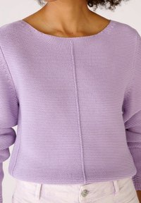 Lavender knit sweater with a wide neckline, textured pattern, and seam details. Paired with light-colored jeans featuring a button.