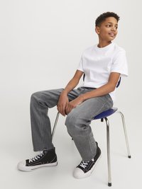 White short-sleeve t-shirt, gray straight-leg jeans, black high-top sneakers with white soles, seated on a chrome-framed blue chair.