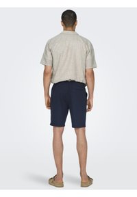 Lys grå kortermet skjorte med en avslappet passform, sammen med marineblå shorts; har en baklomme og uformelle slip-on sko.