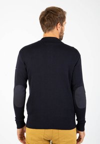 Maglione navy con collo alto, orlo e polsini a coste. Presenta toppe scure sui gomiti, texture lavorata a maglia e design aderente.