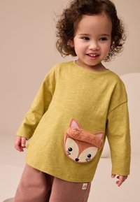 Camicia gialla a maniche lunghe con finitura testurizzata e tasca a forma di volpe. La tasca presenta dettagli ricamati in marrone e beige.