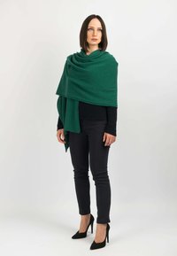 Grøn uldomslag med blød tekstur draperet over skuldrene, parret med en sort top og slanke bukser. Omfatter spidse højhælede sko for et sammenhængende look.