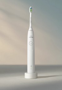 Brosse à dents électrique Sonicare en blanc, avec un design effilé, un bouton d'alimentation et une tête de brosse colorée. Inclut une base de chargement ronde.