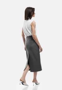 Falda gris hasta la rodilla con una abertura en la parte posterior, combinada con una blusa sin mangas blanca y unas alpargatas perforadas blancas con un pequeño tacón.