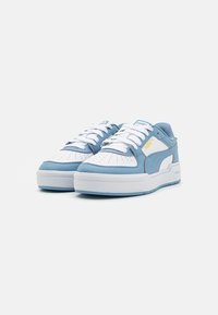 Blauwe sneakers met witte accenten, met een geperforeerde teendoos, dikke witte zool en contrasterende stiksels. Logo aan de zijkant.