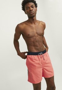 Koraal kleurige zwemboxers met een marineblauwe elastische tailleband, een trekkoordsluiting en zijstrepen, gemaakt van lichte, sneldrogende stof.