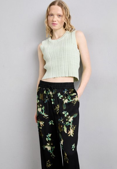 Lys grøn, ribbet, cropped tank top parret med sorte bukser med et farverigt blomsterprint. Glatte teksturer og elastisk talje.