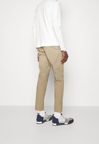 Beige-kardemumma puuvillahousut yhdistettynä pitkähihaiseen valkoiseen paitaan. Jalkineissa on sekoitus harmaata, laivastonsinistä ja valkoista, joissa on nauhakiristys ja teksturoitu pohja.