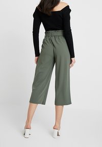 Zelené široké kalhoty na vysoký pas s nařasením, spárované s černým topem bez ramínek a bílými sandály na block heel.