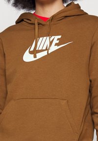 Brun Nike hoodie med en känguruficka, vit logotyp på bröstet, dragsnören vid huvan och ett mjukt, texturerat tyg.
