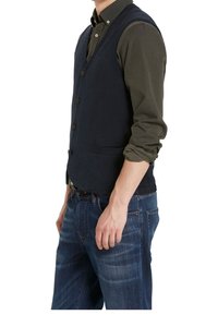 Granatowa wełniana kamizelka z pięcioma guzikami, dwoma przednimi kieszeniami i dopasowanym krojem. Noszona na ciemnozielonej koszuli i w połączeniu z niebieskimi dżinsami.