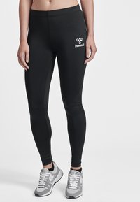 Schwarze Leggings mit einem enganliegenden Design, hergestellt aus dehnbarem Material, mit einem weißen Logo am Oberschenkel und einer glatten Textur.