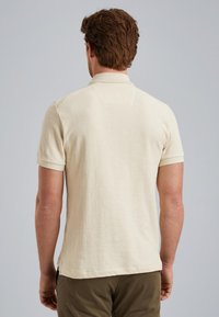 Kurzarmpolohemd aus beigem Stoff mit texturiertem Finish und traditionellem Kragen. Die Rückseite hat eine dezente Nahtdetails.