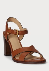 Hnedé kožené sandále na podpätku s prekríženými pásikmi, nastaviteľným remienkom na členku a dreveným blokovým podpätkom pre podporu a stabilitu.